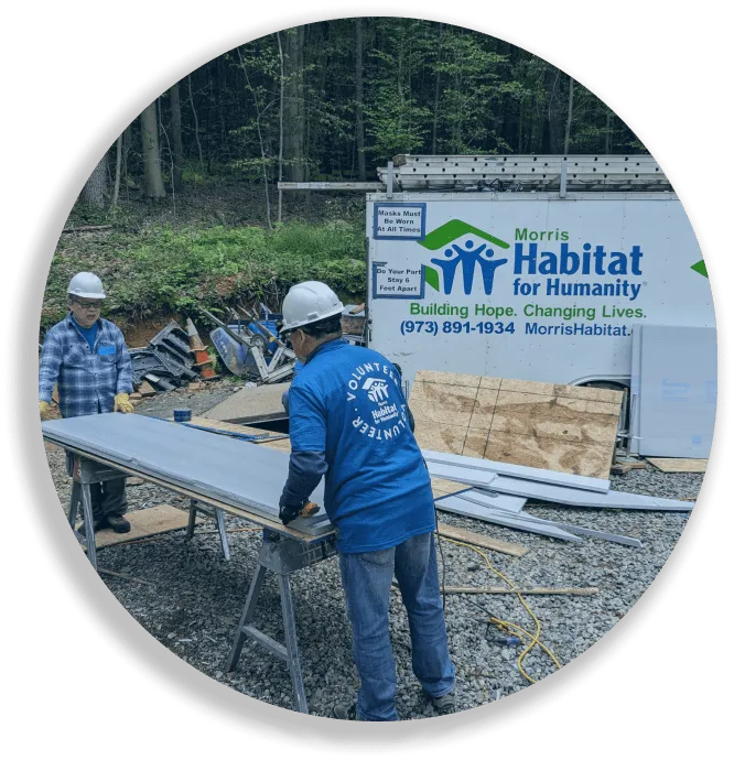Two construction volunteers working with metal sheets near a Morris Habitat for Humanity trailer.