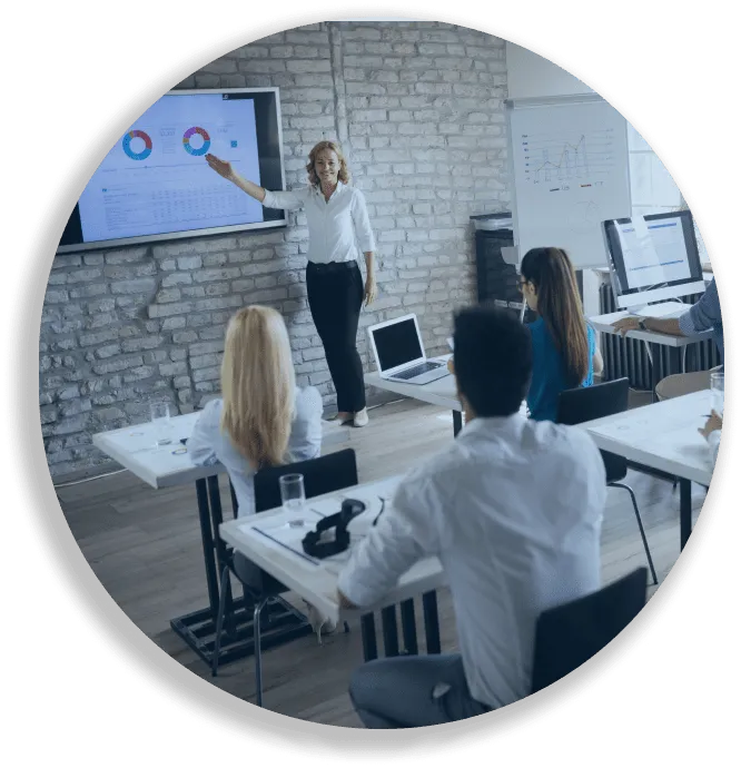 Woman presenting data charts on a screen to a group seated in a modern office classroom.
