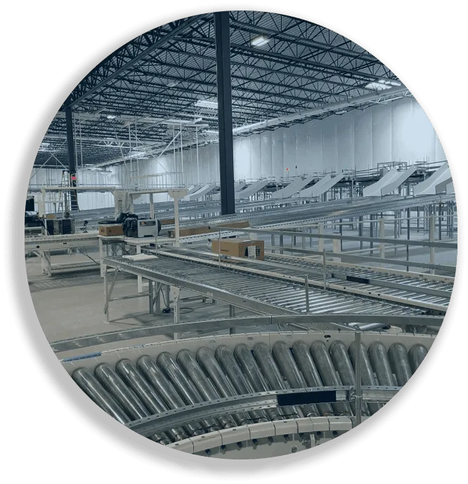 Large empty warehouse with metal conveyor belts and rolling tracks for package sorting or assembly.