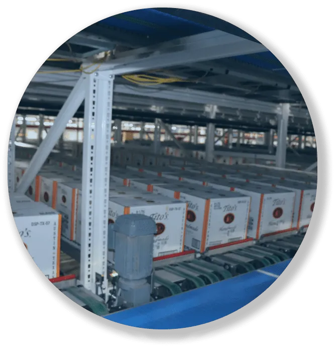 Stacked cartons on conveyors inside an industrial warehouse with metal shelving and machinery.