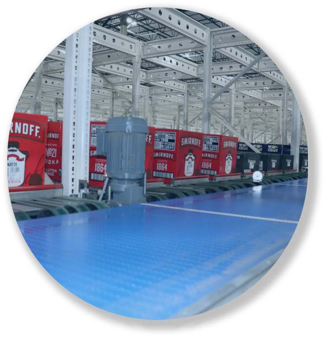 Conveyor belt with Smirnoff vodka cases in a warehouse with white metal shelving.