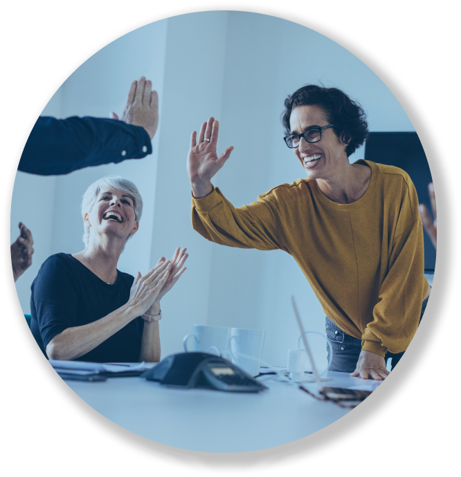 Two women smiling and high-fiving in an office setting while another applauds nearby.