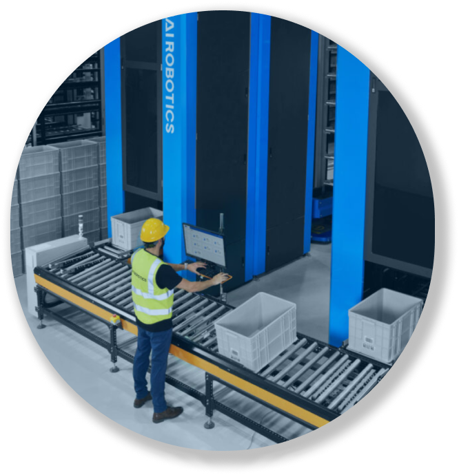 Worker in a yellow helmet and vest operating a control panel by an automated conveyor system in a warehouse.
