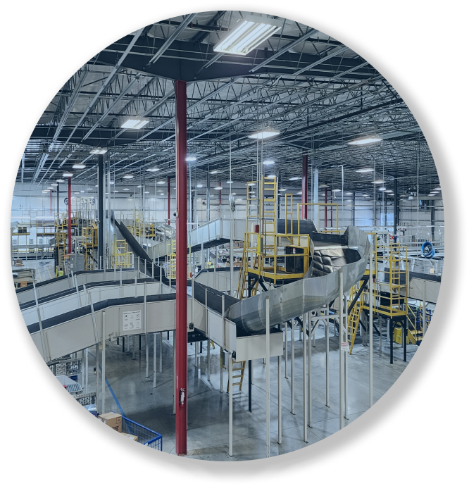 Large industrial warehouse with conveyor belts and metal platforms under bright overhead lights.