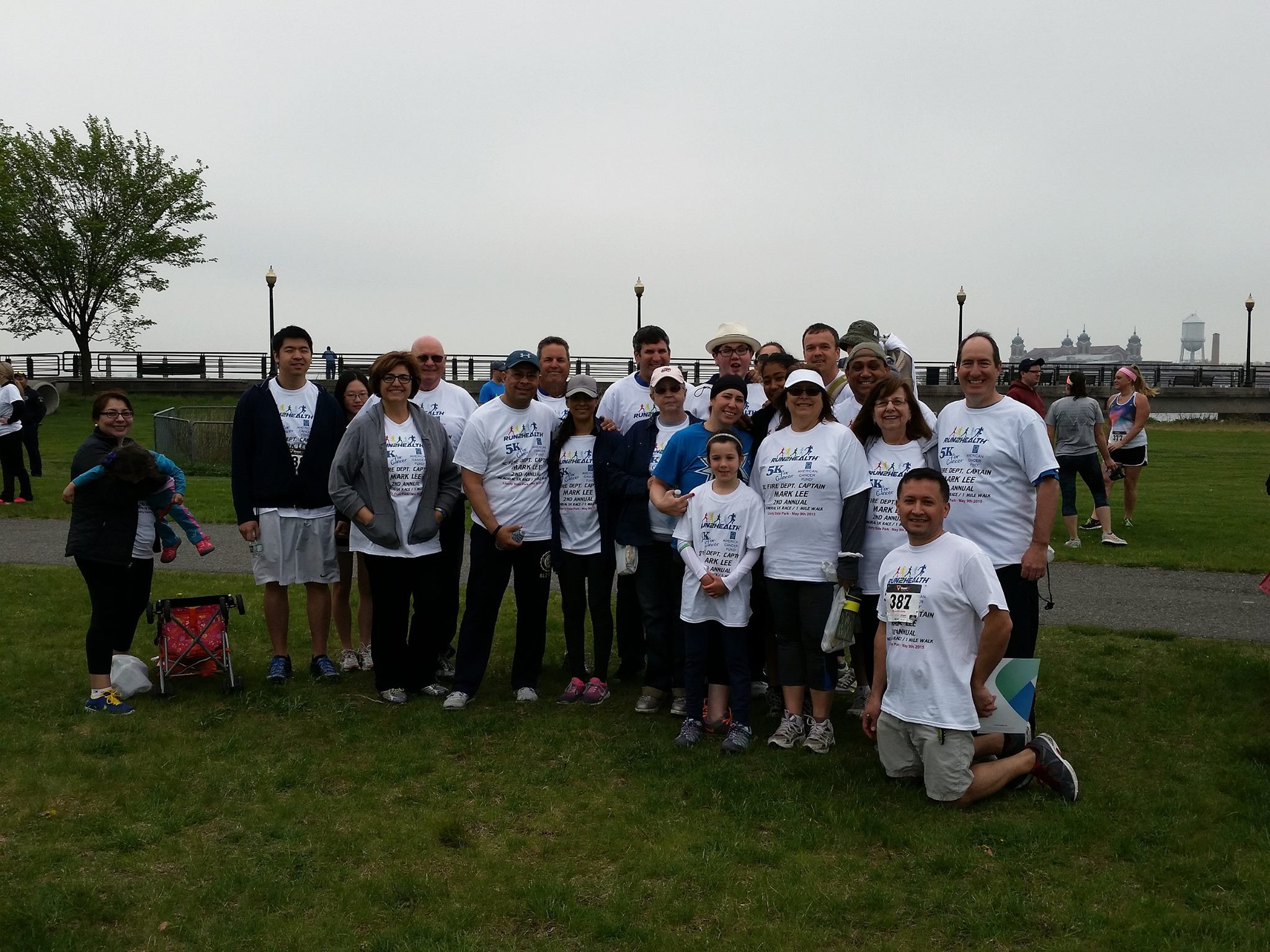 Group of people wearing matching charity run shirts posing for photo on grassy park on cloudy day.