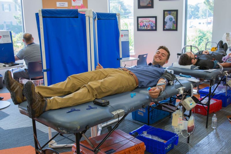 Two men lying on beds donating blood indoors, one smiling at the camera.