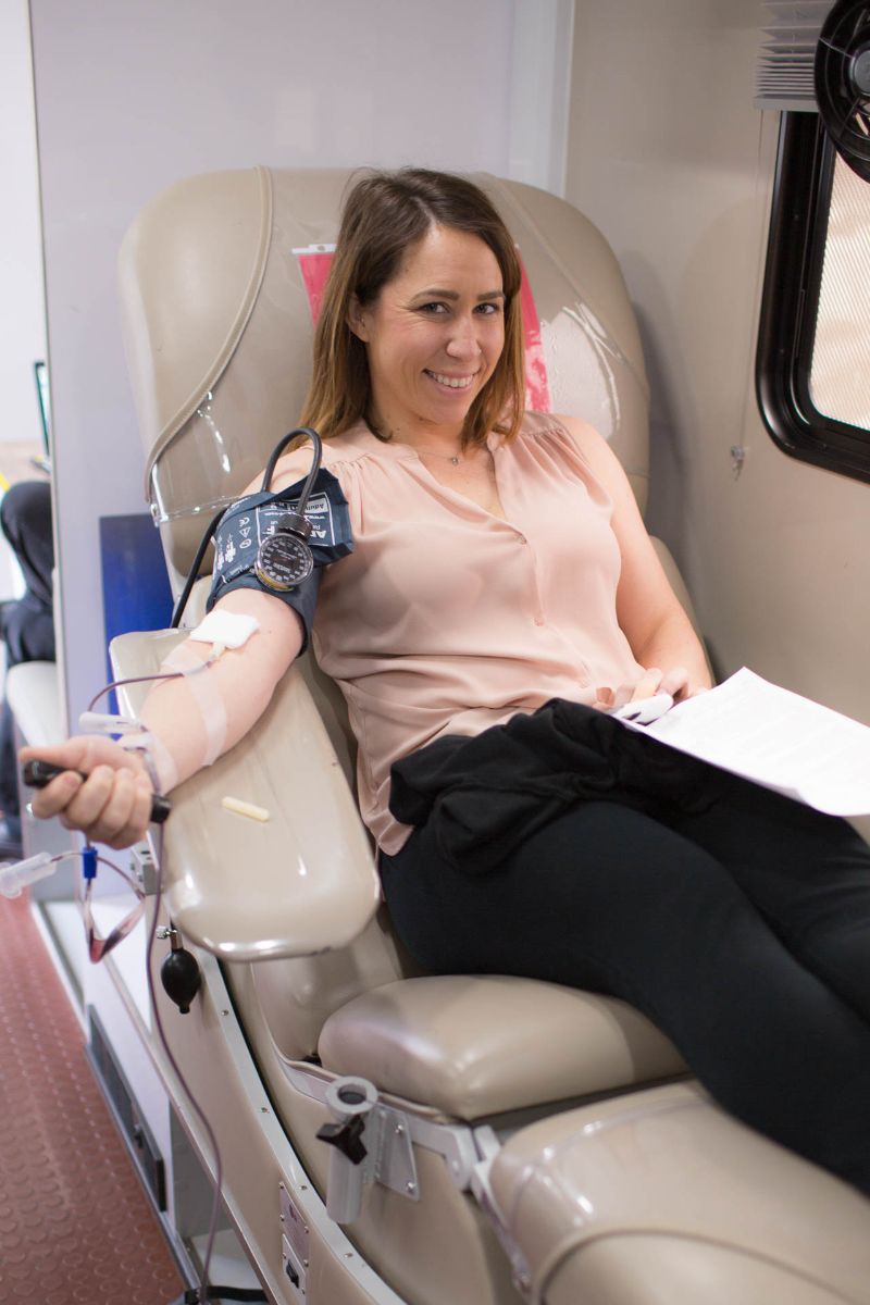 Smiling woman donating blood while seated in a medical chair inside a blood donation vehicle.
