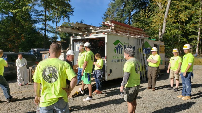 Volunteers in bright shirts and helmets gathered near a Habitat for Humanity truck outdoors.