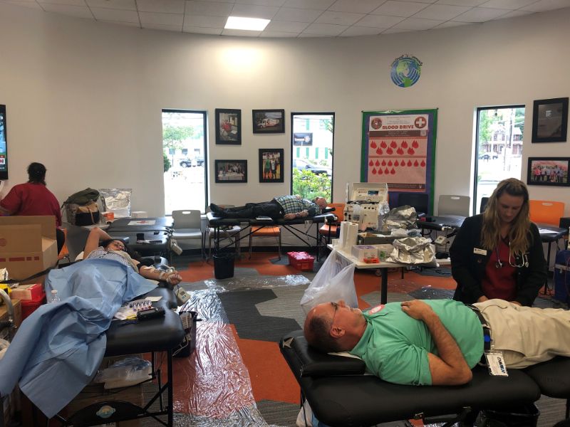Multiple people lying on beds donating blood in a clinic room with medical staff attending.