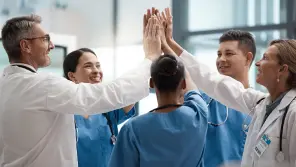 Group of five diverse healthcare professionals giving each other a high-five in a hospital hallway.