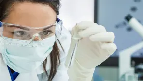 Scientist wearing safety glasses and mask holds a test tube in a laboratory.