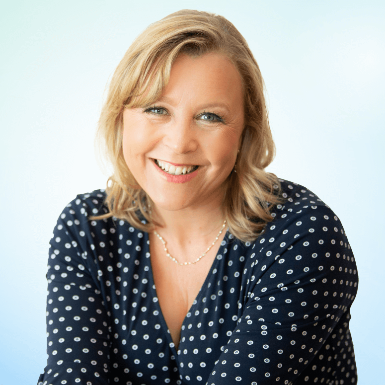 Smiling woman with blonde hair wearing a navy blue blouse with white circular patterns, against a light blue gradient background.