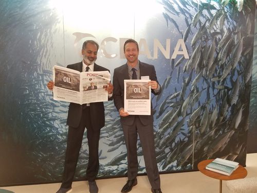 Two men in suits holding up newspapers with headline "Spoiled" in front of a fish mural.