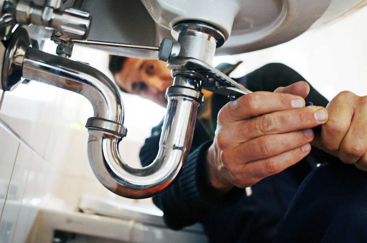 A plumber tightening a sink trap during a maintenance call