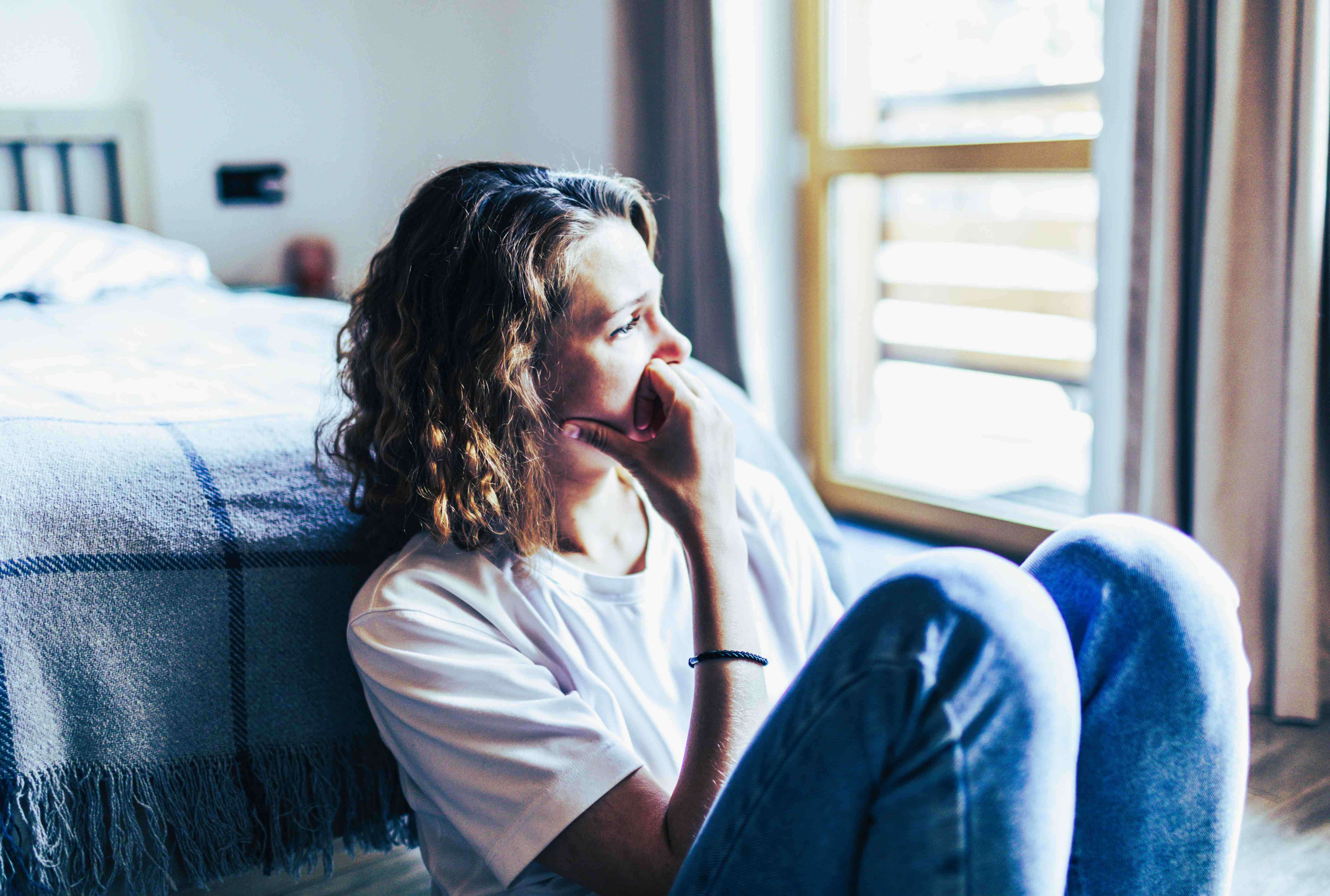 woman sitting next to bed and starring out the window
