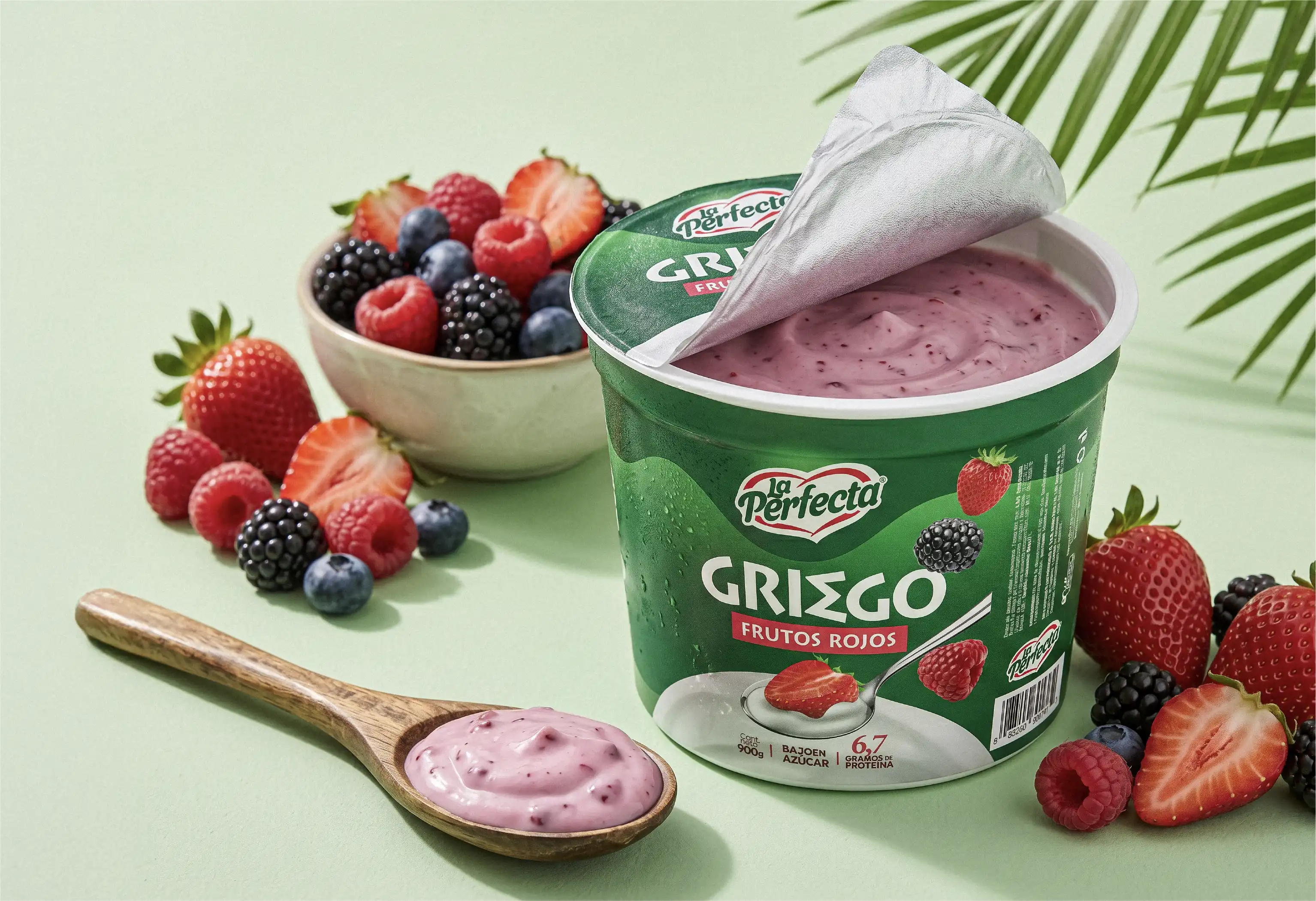 Pote de yogur griego La Perfecta sabor frutos rojos, bajo en azúcar y con 6.7 g de proteína, rodeado de fresas, moras, arándanos y frambuesas, campaña Más natural