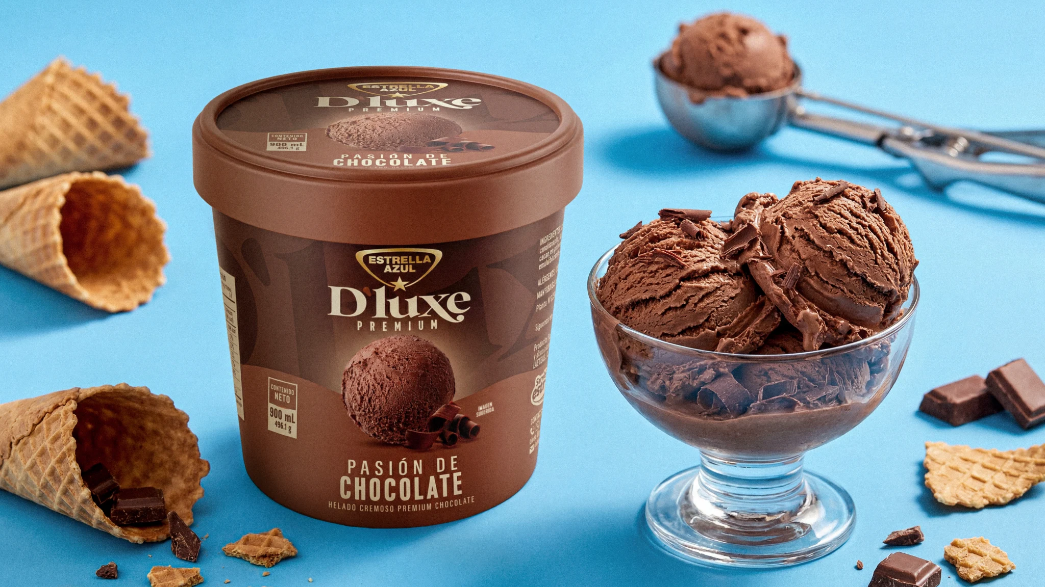 Helado D'luxe Pasión de Chocolate junto a copa con bolas de helado, conos de waffle y trozos de chocolate sobre fondo azul
