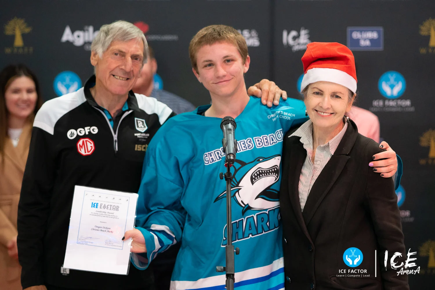 Young Ice Factor participant holding a certificate beside two adult supporters at a community event, reflecting achievement, encouragement and renewed connection through sport.