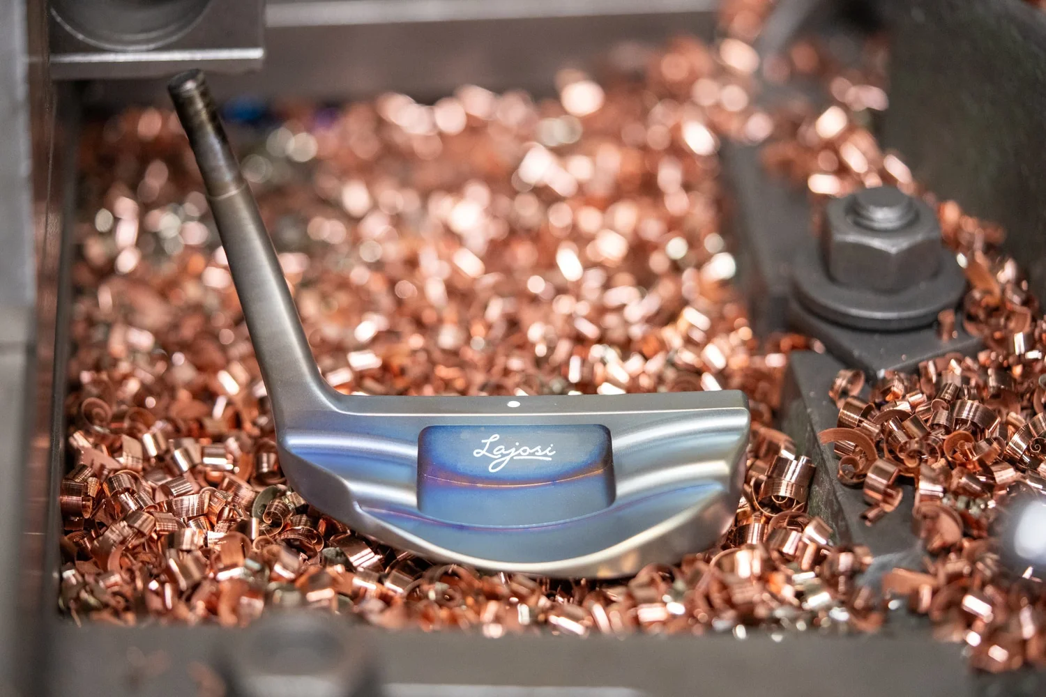 Handcrafted Lajosi putter resting among copper machining shavings in the workshop, highlighting the precision, materials and maker-led craftsmanship behind each custom club.