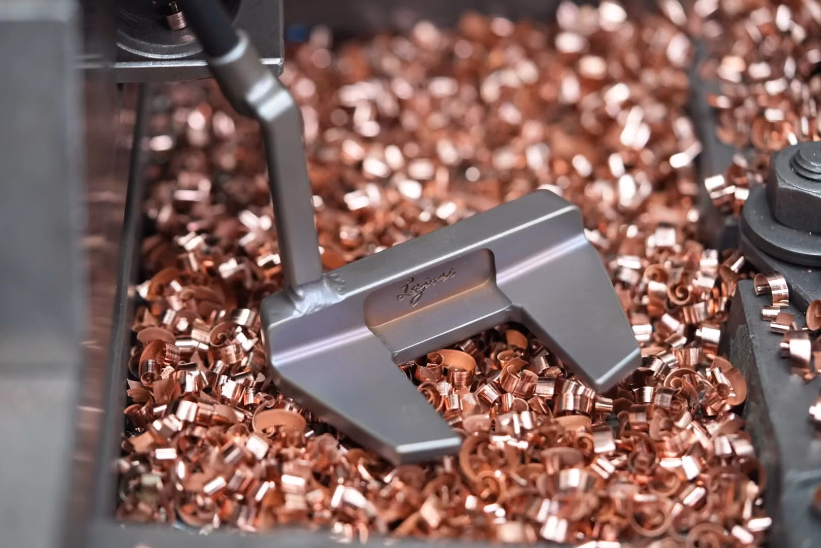 Handcrafted Lajosi mallet putter resting among copper machining shavings in the workshop, highlighting its precision milling, custom finish and maker-led craftsmanship.