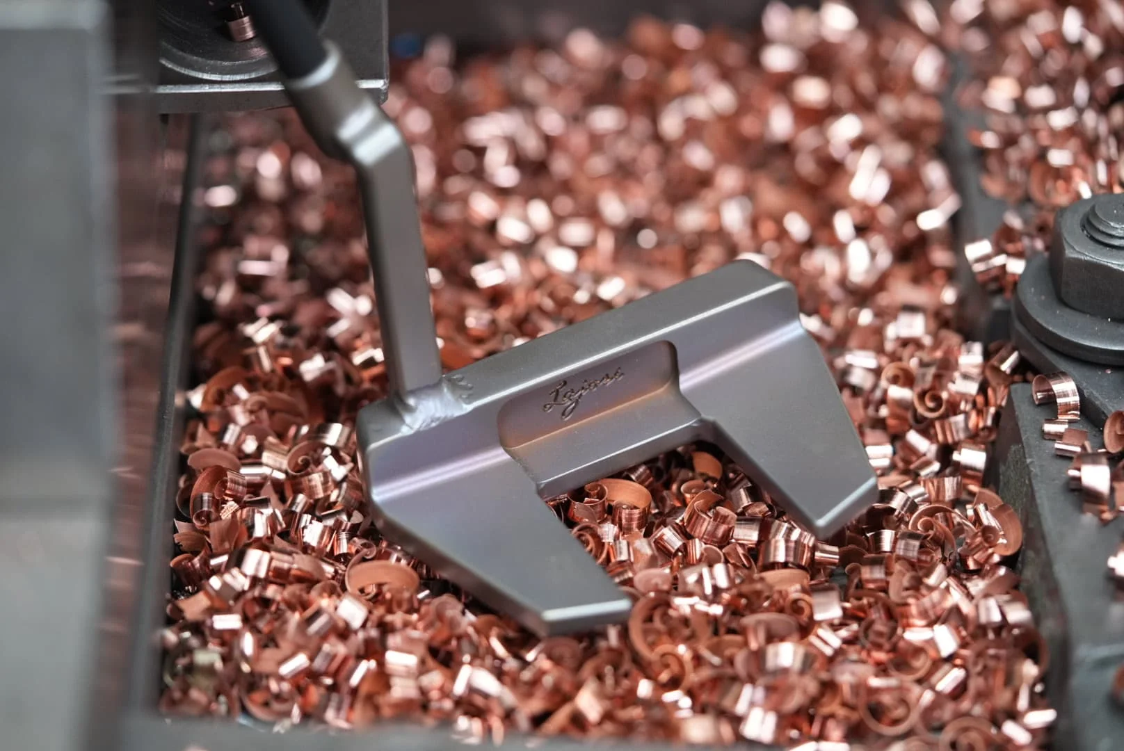 Handcrafted Lajosi mallet putter resting among copper machining shavings in the workshop, highlighting its precision milling, custom finish and maker-led craftsmanship.