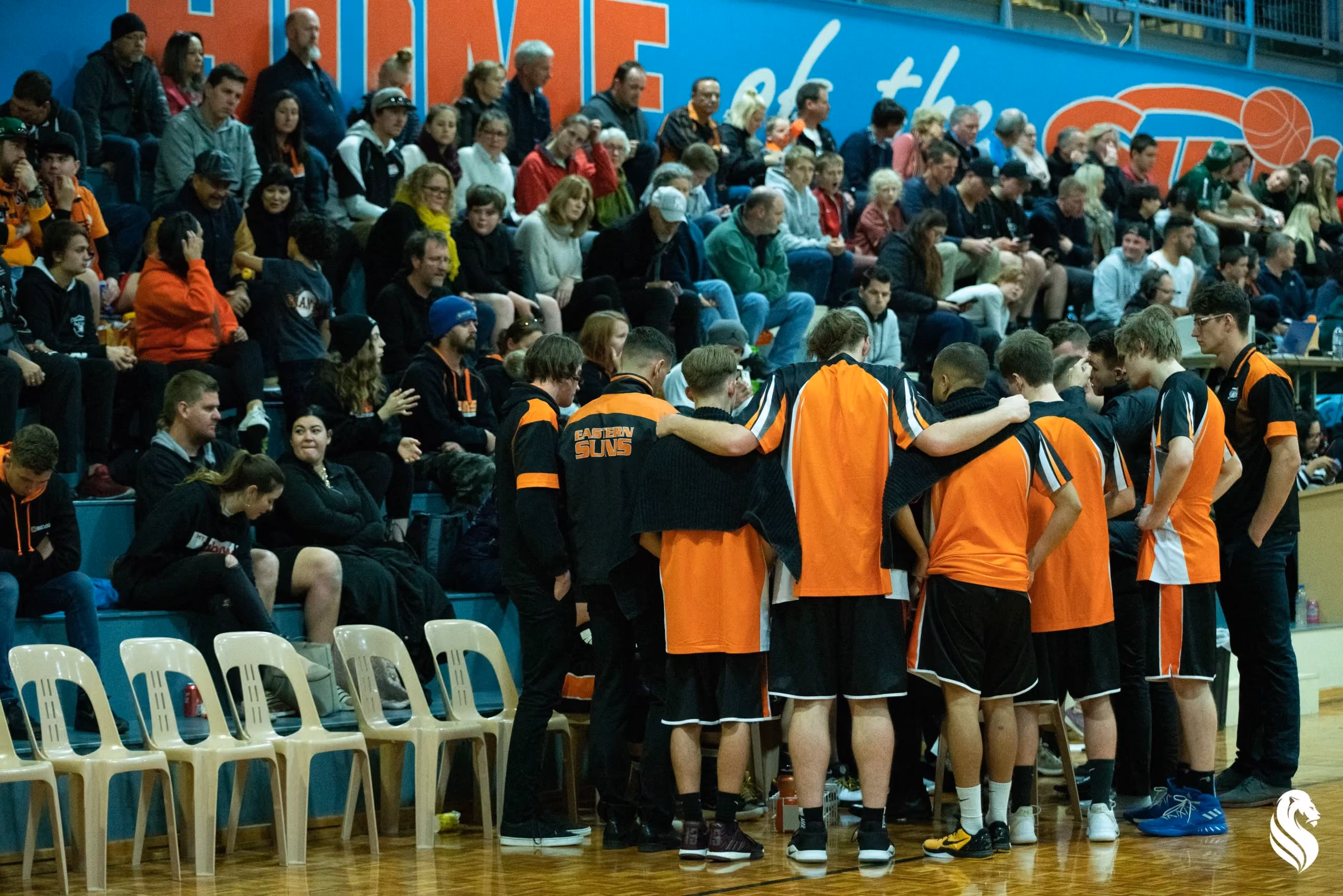 Kalamunda Eastern Suns players huddle courtside in front of a packed home crowd, showing the stronger game-day atmosphere and community momentum built around the club.