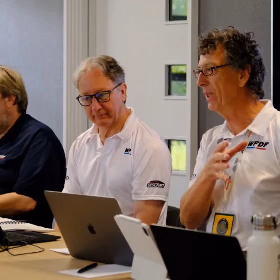 Aussie Open event officials meet around laptops and tablets, reflecting the planning, coordination and professional event structure supporting the tournament.