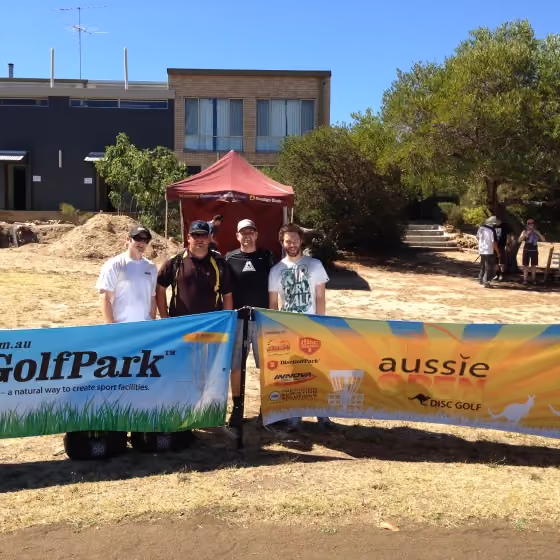 Four Aussie Open organisers and participants stand behind event and sponsor banners at the Mundaring course, reflecting the community support and local partnerships behind the tournament.