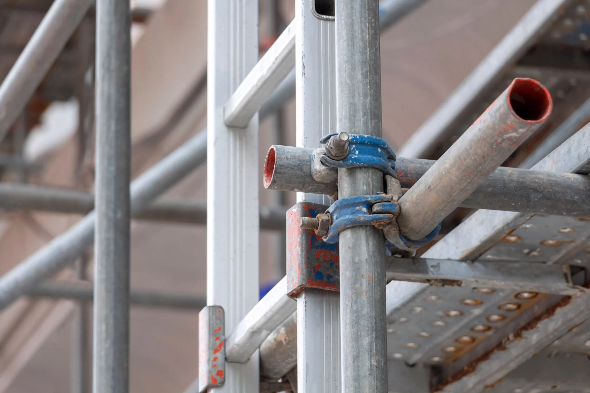 Close-up of scaffold tubes secured with metal couplers beside an access ladder, highlighting the practical safety and structural detail behind reliable commercial scaffolding.