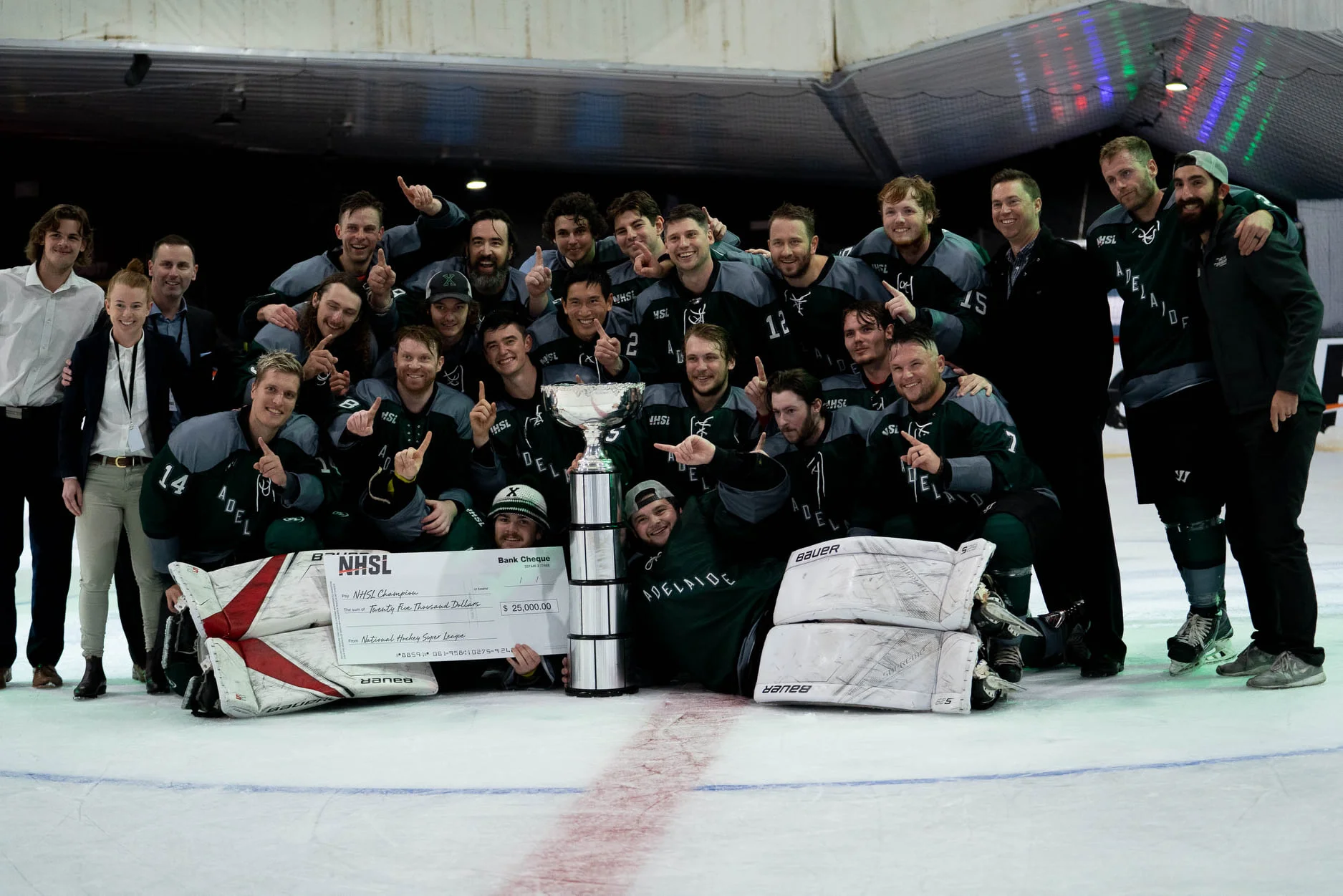 NHSL championship team celebrating on the ice with the league trophy and prize cheque, showing the credibility, player opportunity and shared identity created by the new national competition.