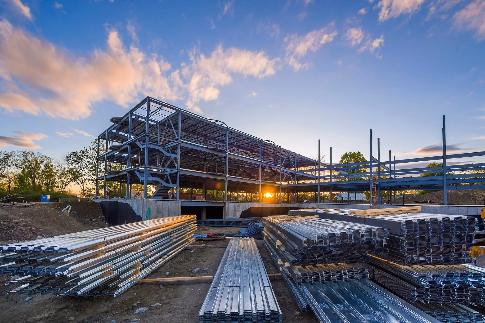 Steel-framed commercial building under construction with stacked materials in the foreground, highlighting the scale and coordination involved in larger commercial projects.