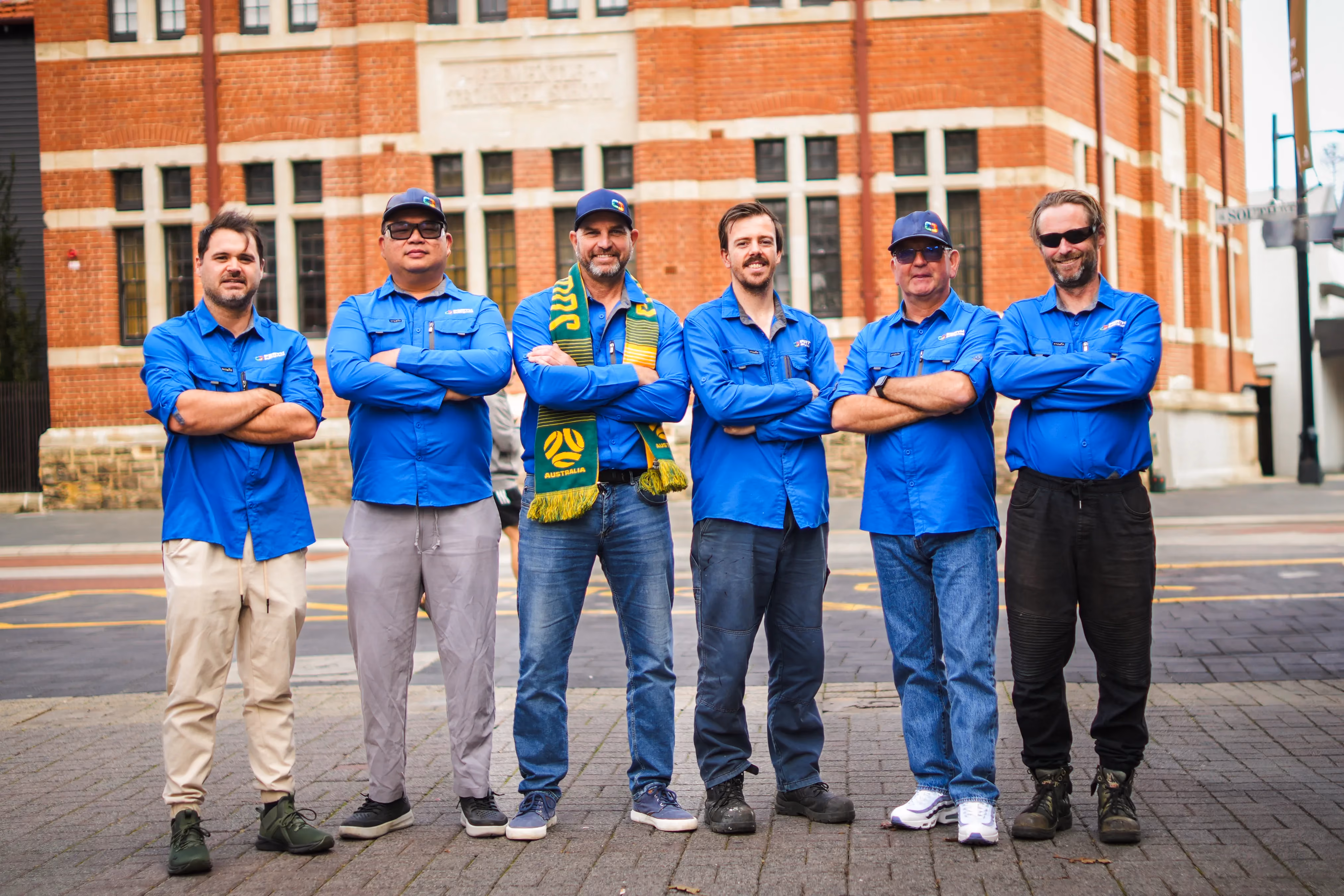 Perth Surveying team members stand together in branded blue uniforms outside a heritage building, presenting a capable, approachable team behind the company’s reliable local service.