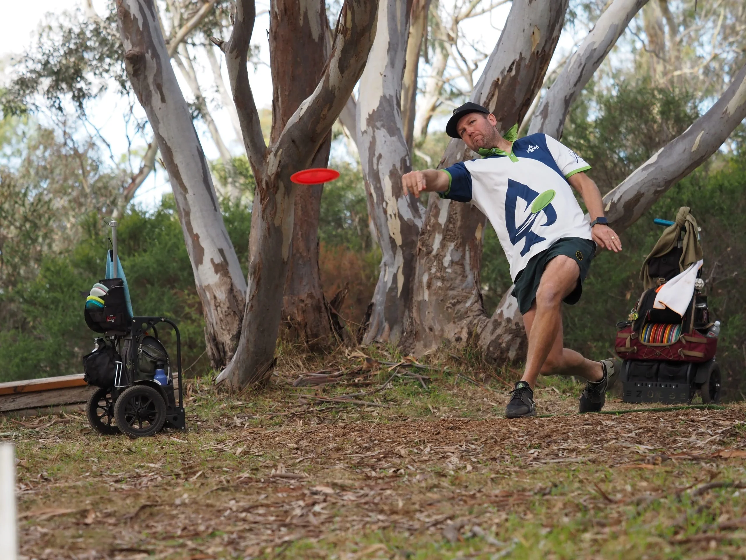 Team Aces disc golfer releases a red disc on a wooded course, capturing the athlete-led action and recognisable brand content used to strengthen engagement and community connection.