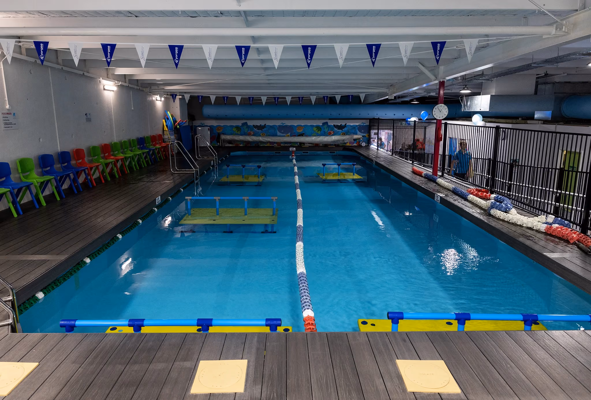 Wide view of the WaterPonyz indoor swimming pool with lane ropes, training platforms and colourful children’s seating, showing the structured, safe and family-focused environment behind the school’s enrolment journey.