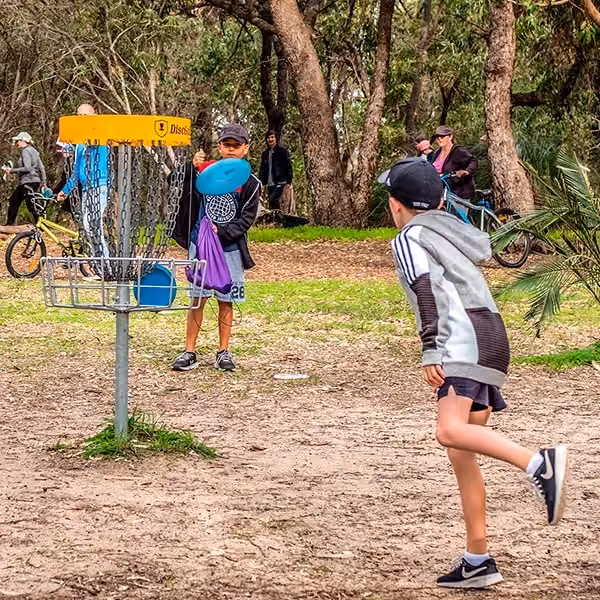 Children playing disc golf at a community park basket, reflecting the sport's fast-growing local demand.