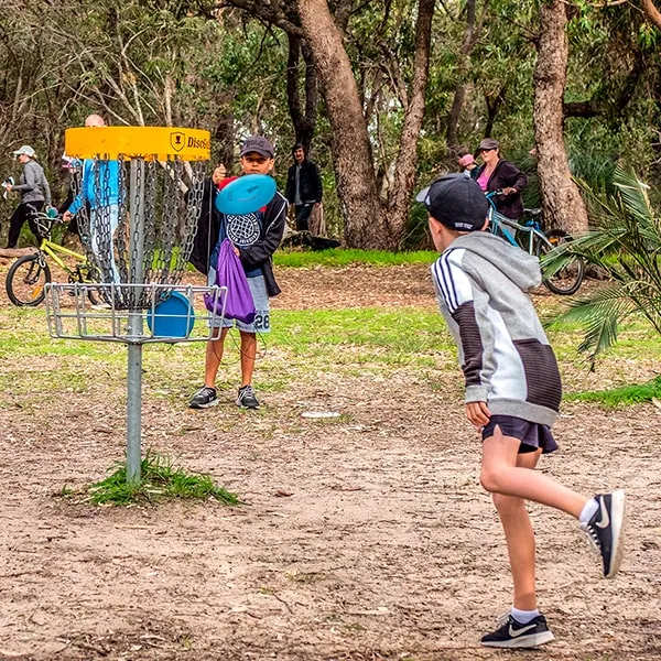 Children playing disc golf at a community park basket, reflecting the sport's fast-growing local demand.