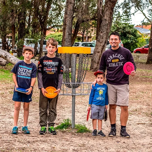 A father and three children standing at a disc golf basket after a round, holding their discs.