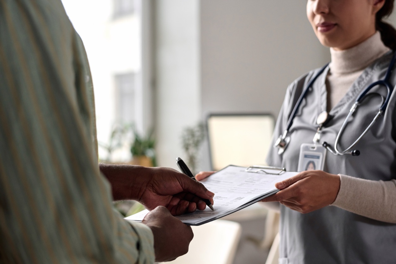 Close-up of a healthcare professional holding a clipboard as a person signs a document with a pen in a well-lit room.