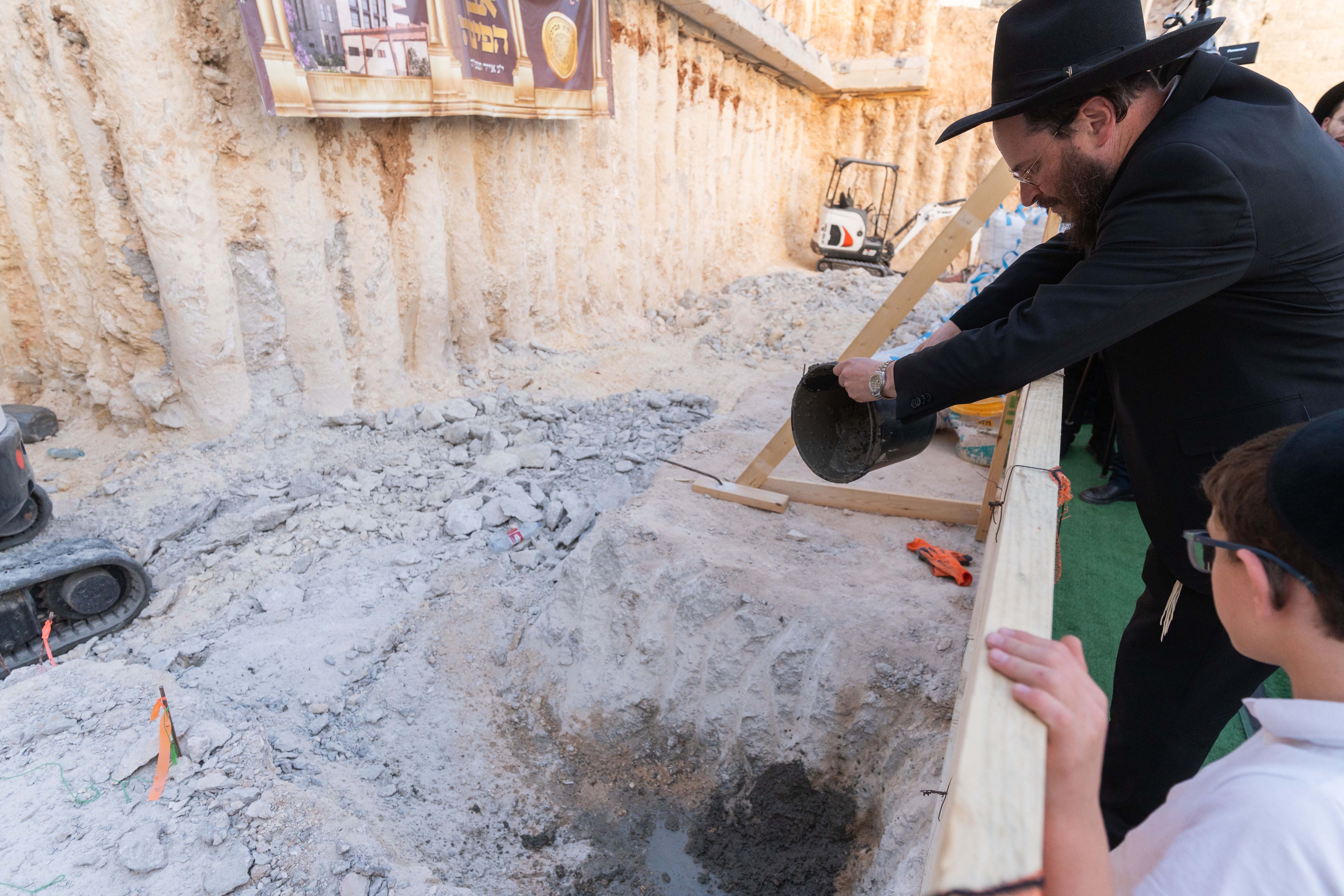 Man in black hat pouring concrete into a construction pit while a boy watches nearby.