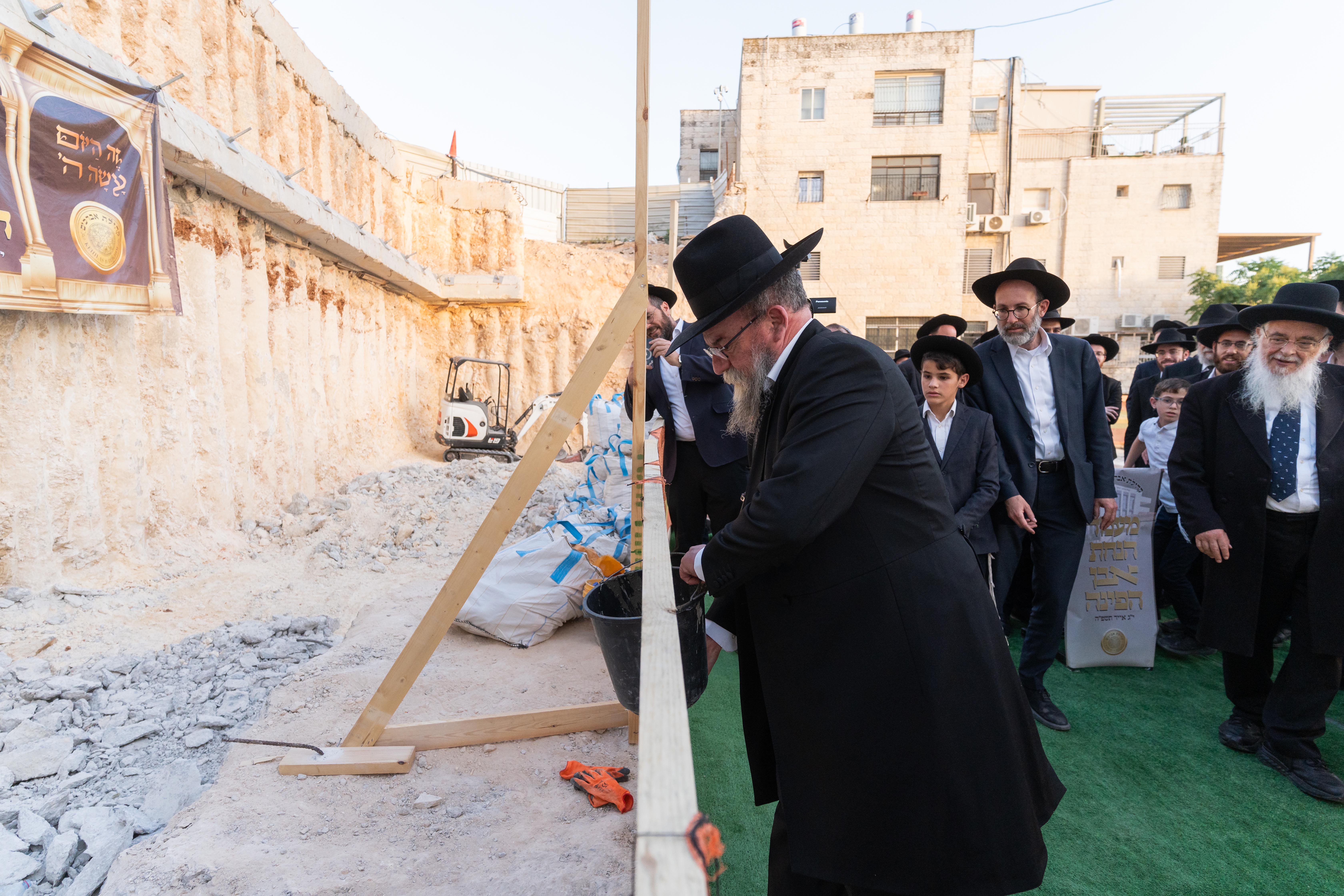 Group of men, many in traditional Jewish attire, gathered near a construction site wall.