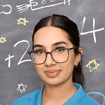 Miss Mahima Willunga Child Care Educator with glasses and a blue shirt standing in front of a chalkboard with mathematical drawings and stars.