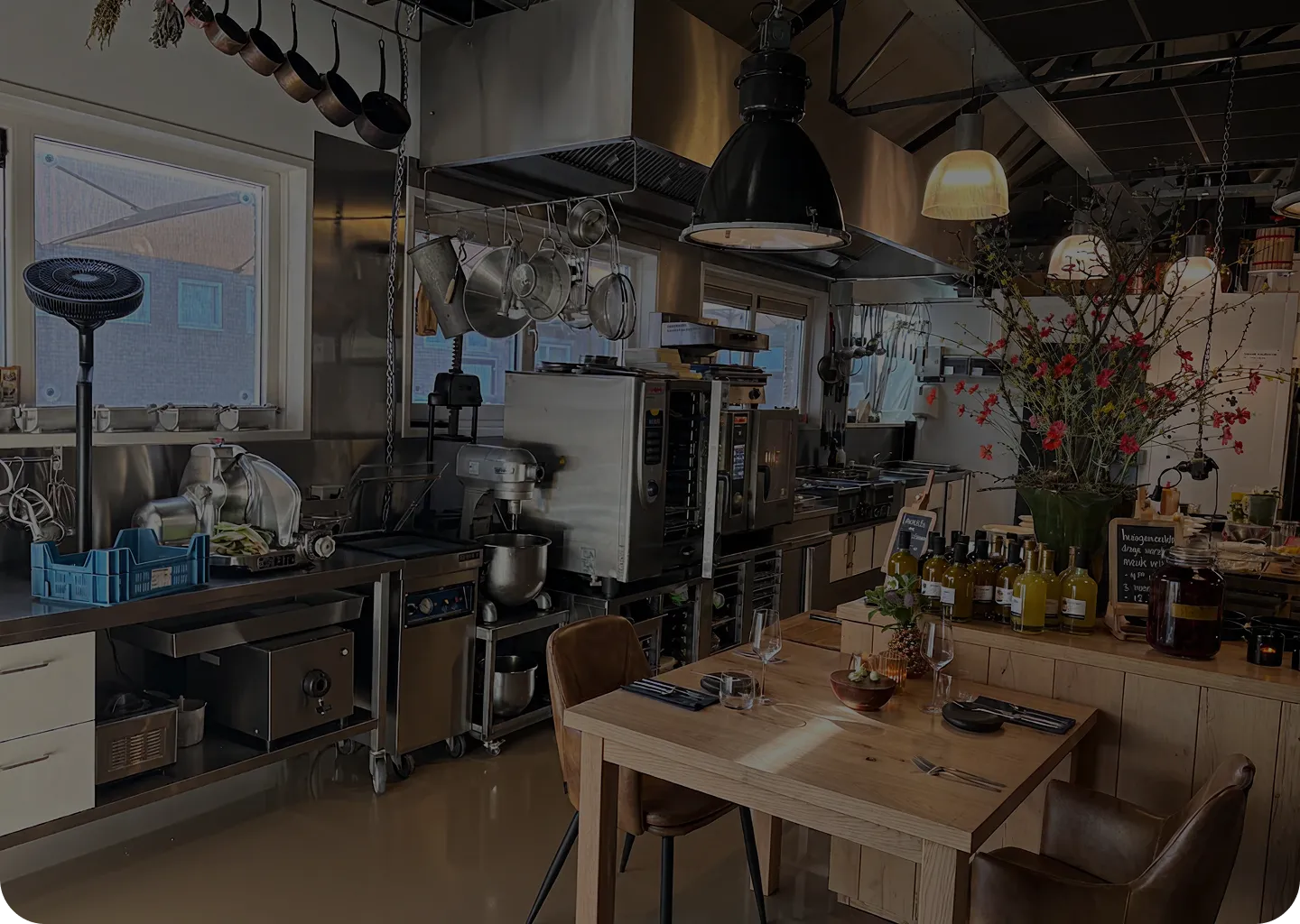 Modern commercial kitchen with stainless steel appliances and a wooden dining table set for two.