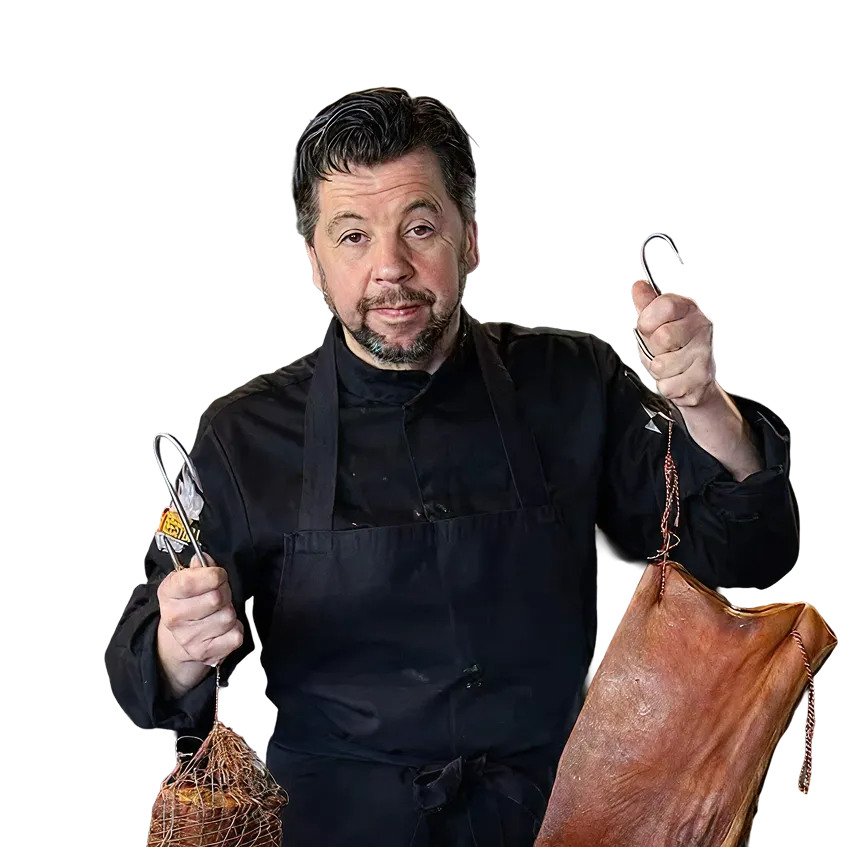 Man in black chef outfit holding a cured meat hanging in each hand with hooks.
