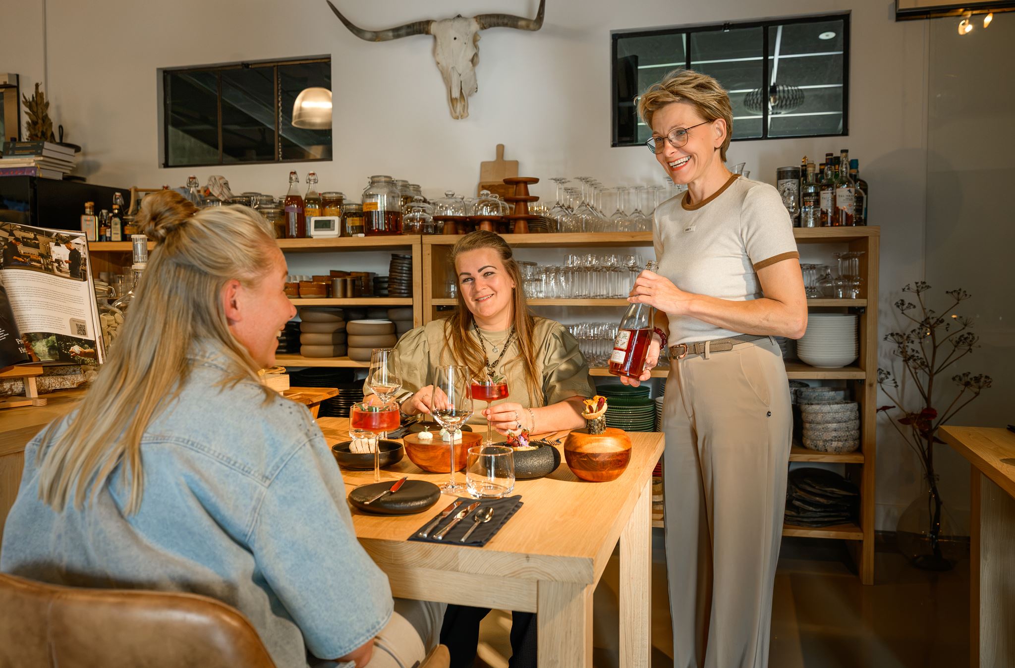Three women enjoying drinks and desserts at a wooden table in a cozy restaurant setting.