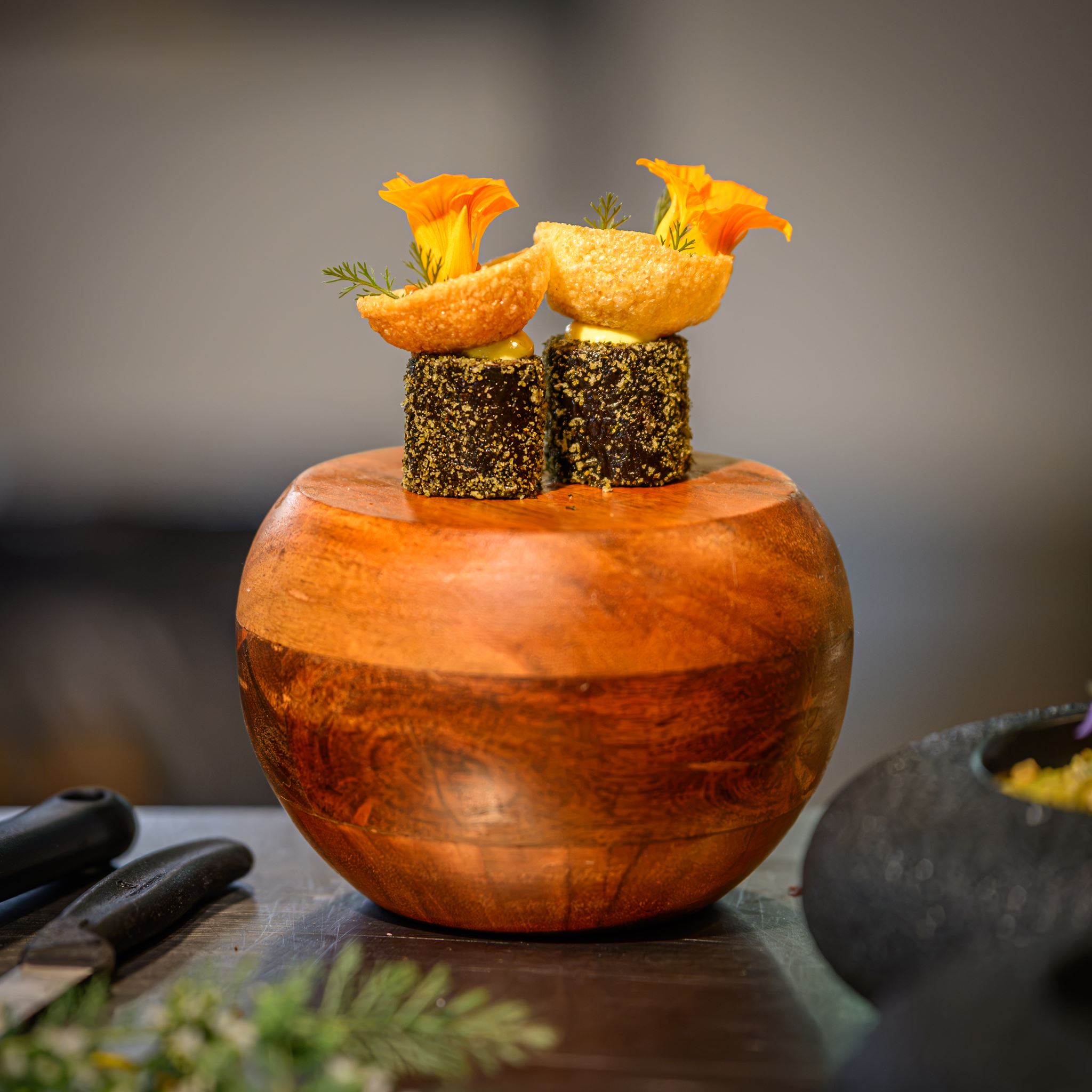 Two gourmet appetizers with orange edible flowers on a round wooden serving bowl.