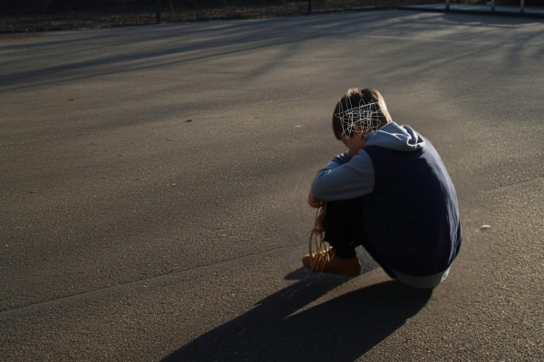 A sad 8 year old boy sat by himself on the school playground.