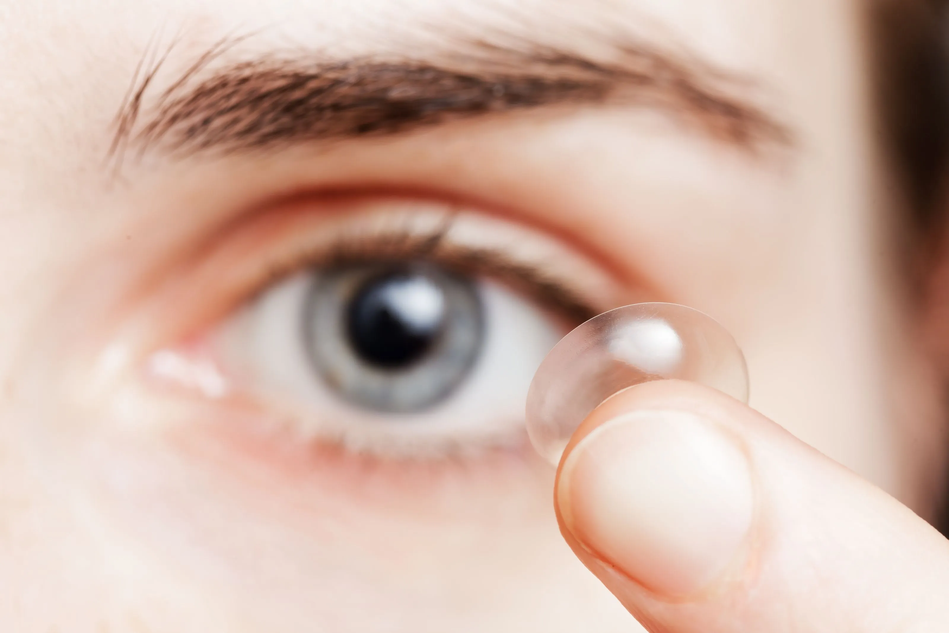 Close-up of a person holding a clear contact lens near their eye.