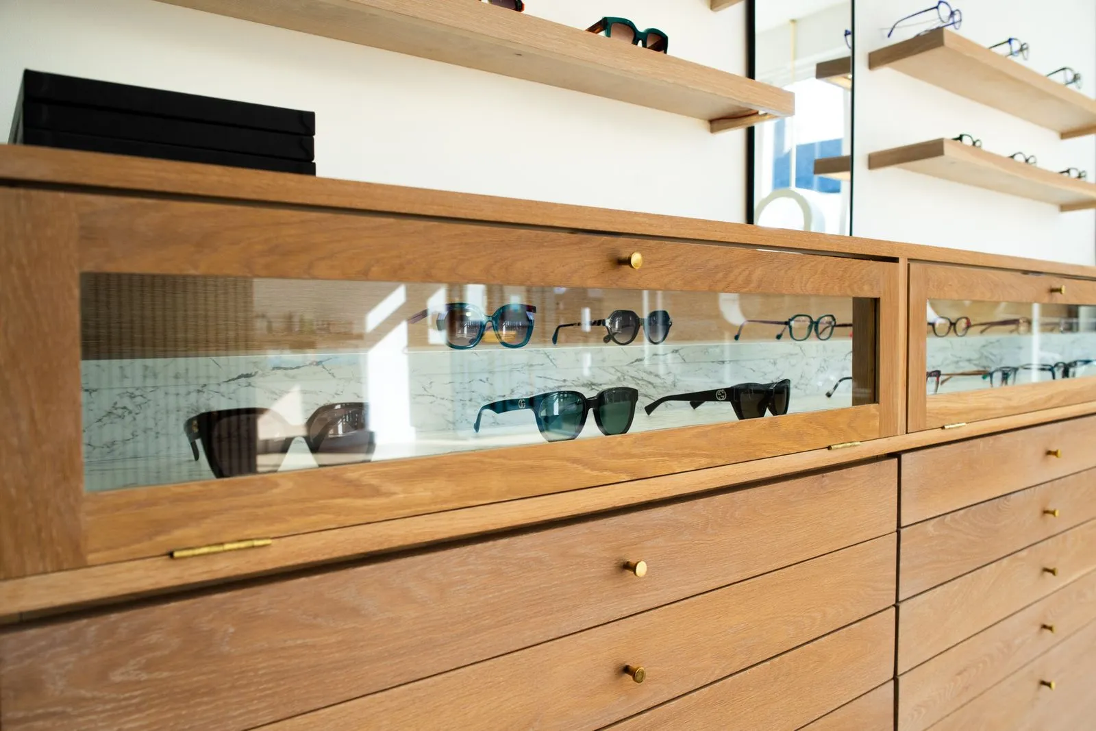 Wooden display cabinet with glass cases showcasing various designer sunglasses