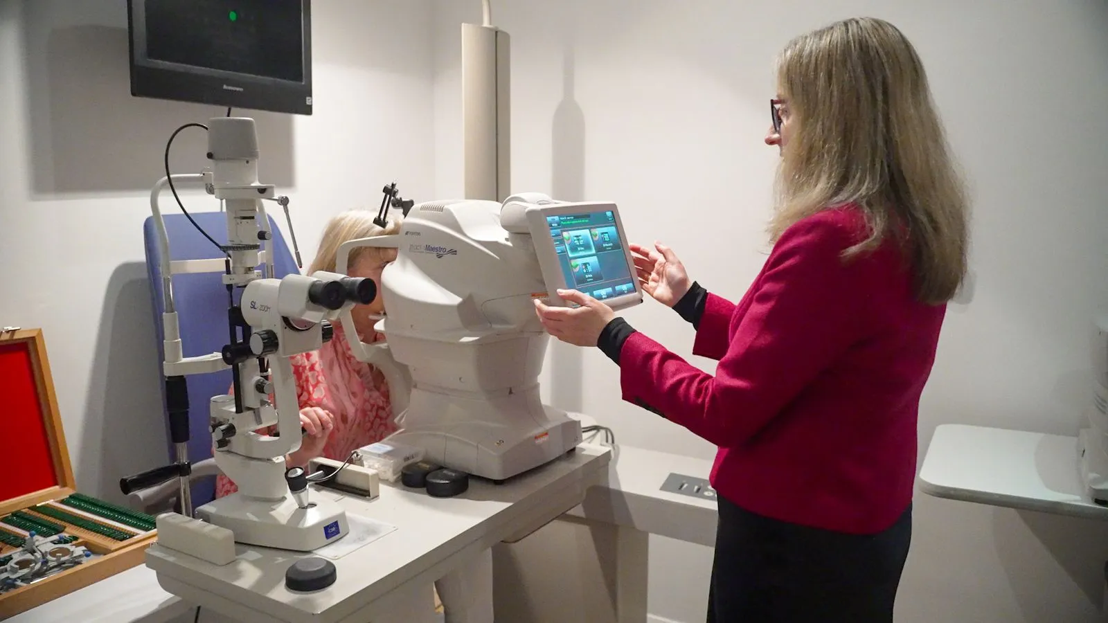 Eye care professional operating diagnostic machine while patient looks into eye examination device.