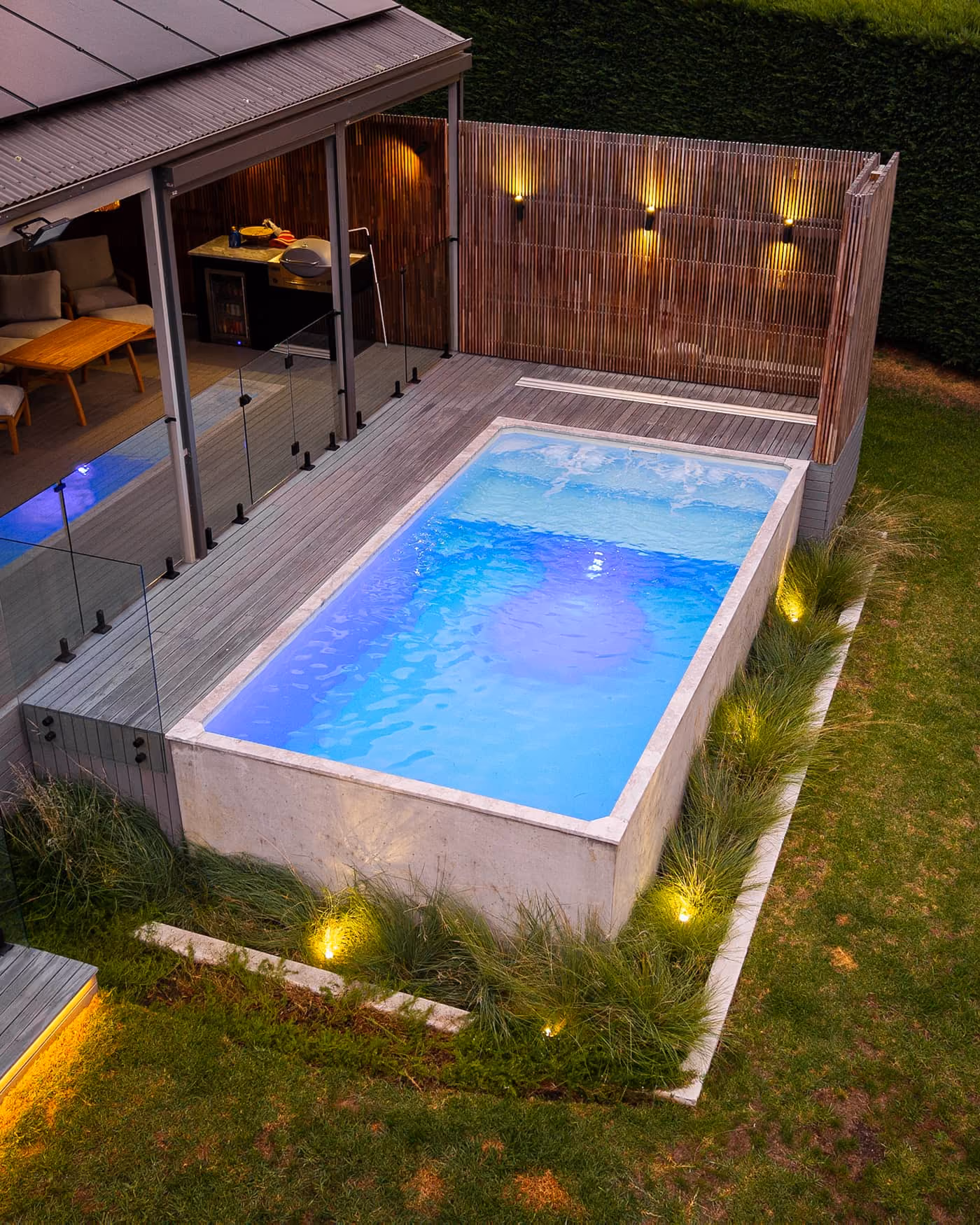 Modern outdoor swimming pool beside a covered alfresco entertaining area with glass balustrades. The spacious roofed patio creates a seamless indoor-outdoor living space ideal for year-round entertaining.